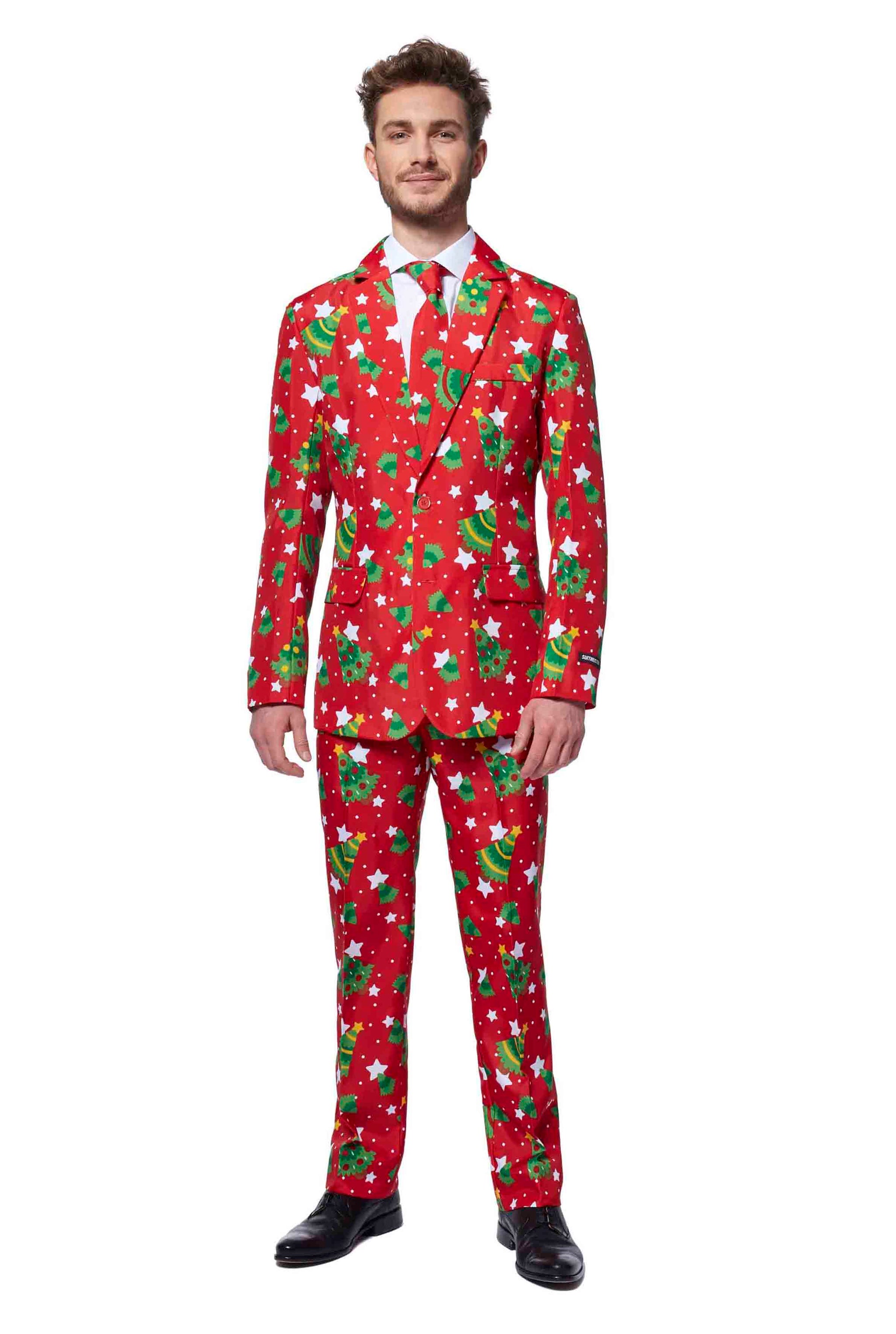 A man wearing the Suitmeister Christmas Trees Stars Red suit stands smiling. The festive ensemble includes patterns of trees and stars, complemented by a white shirt, red tie, and black shoes.