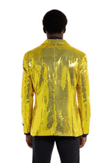 A person wearing a Suitmeister Sequins Blazer in vibrant yellow stands with their back to the camera. The blazer reflects light, creating a bold, shimmering effect. The person is also wearing dark pants.