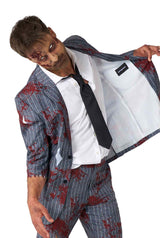 A person dressed in the Suitmeister "Zombie Grey" costume is wearing a pinstriped suit with faux blood stains, paired with a white shirt and black tie. They have zombie makeup featuring artificial wounds and are pulling one side of the suit open to showcase the lining.