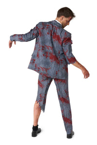 A person dressed in the Zombie Grey - Zombie costume by Suitmeister poses against a white background. The suit, with its tattered sleeves and pants giving it a ragged look, is designed to appear blood-stained and striped. The individual stands with their back turned slightly to the camera.